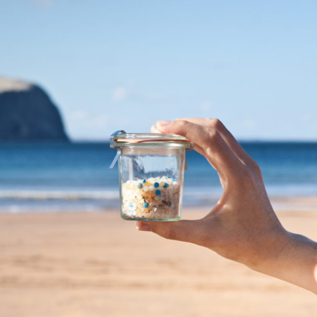 Hand holding a jar full of plastic polution (nurdles) on a beach